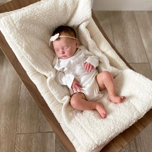 Poupée Reborn dormant sur un transat en bois rembourré beige avec une couverture blanche