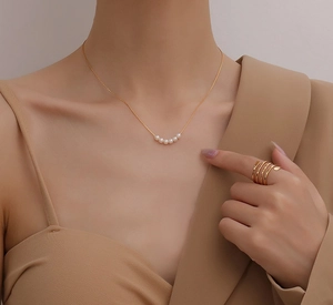 Detail einer natürlichen Süßwasserperlenkette und eines goldene Spiralrings am Modell