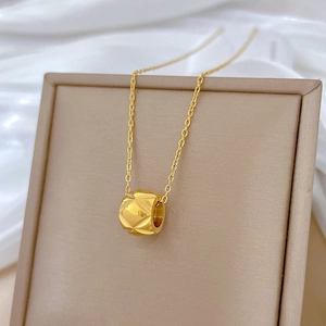 Detailed close-up of gold titanium necklace with rhombus textured cylinder on silk fabric