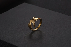 Close-up of a gold lightning bolt ring made of polished stainless steel on a dark pedestal