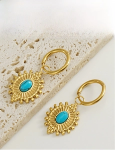 Détail de boucles d'oreilles turquoise au design soleil sur socle en pierre blanche