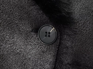 Macro view of black winter coat featuring suede texture, round button, and faux fur lining