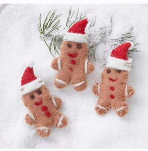 Close-up of three wool felt gingerbread man ornaments with green pine branches