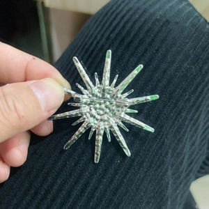 Silver starburst brooch with sparkling rhinestones shown on a dark fabric background