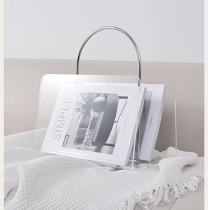Detail of transparent acrylic magazine rack with silver metal curved handle on white fabric