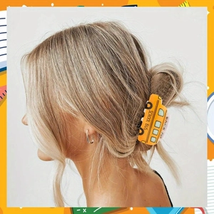 Détail de la pince à cheveux bus scolaire jaune avec lettrage noir sur une coiffure chignon