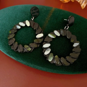 Detailed close-up of circular geometric earrings with green shell inlay on green velvet