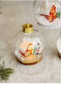Detalle de bola de Navidad LED con mini casa de madera, muñeco de nieve y nieve artificial