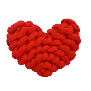 Detail of a handmade red heart-shaped knotted pillow with soft knitted texture