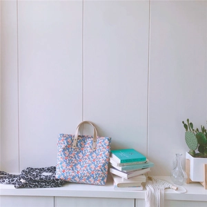 Dettaglio borsa tote in cotone floreale con manici in pelle su superficie bianca