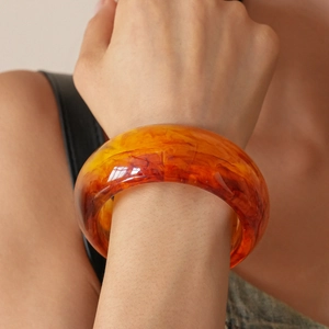 Close-up of amber resin geometric bangle with orange swirl texture on woman wrist