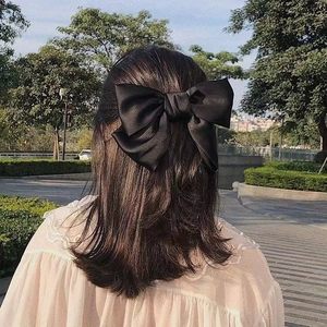 Detail of a large black satin bow hair clip styled on a half-up hairstyle in natural light