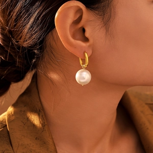 U-shaped gold drop earrings featuring large white pearls worn on a model's ear