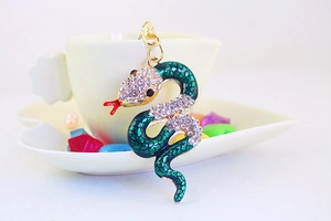 Macro shot of green enamel snake keychain with sparkling rhinestones on a coffee cup