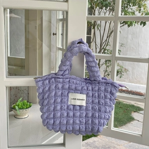 Detail of purple textured bubble fabric handbag with woven brand label against garden view