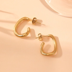 Macro detail of twisted gold U-shaped stainless steel earrings on warm fabric