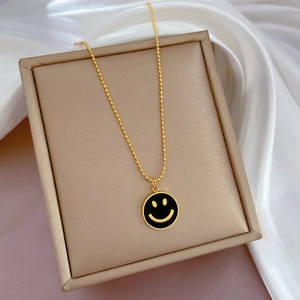Nahaufnahme einer vergoldeten Titanstahl-Halskette mit schwarzem Smiley-Anhänger auf Seide
