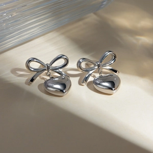 Macro detail of silver stainless steel bow earrings with 3D heart-shaped pendants