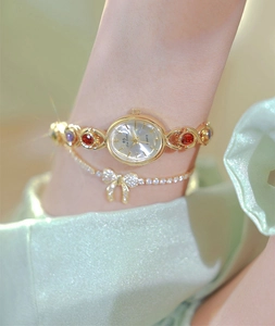 Close-up of gold oval quartz watch with red and blue gemstones and bow bracelet