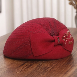 Detail of burgundy wool beret with mesh veil, oversized bow and beadwork on wood surface