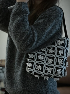 Detailed close-up of intricate white floral embroidery on a vintage black canvas shoulder bag