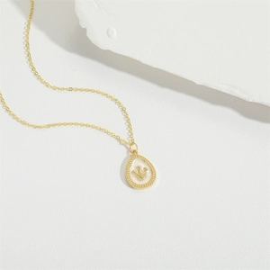 Minimalist gold necklace with drop pendant and crown motif on white stone background
