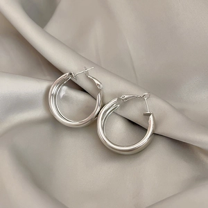 Polished silver metal hoop earrings resting on elegant beige silk fabric texture