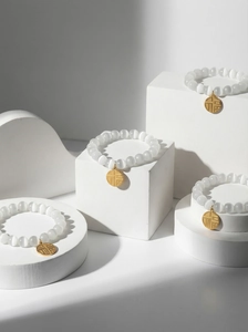 Macro detail of white cat-eye bead bracelets with gold Fu pendant on geometric blocks