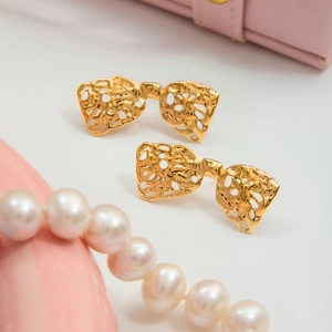 Detail of gold hollow bow earrings with lace texture on pink jewelry box with pearls