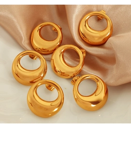 Macro shot of three pairs of golden hollow hoop earrings on elegant champagne silk fabric