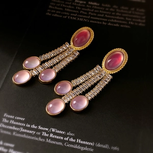 Dettaglio ravvicinato di orecchini vintage con nappe e zirconi rosa su sfondo di libro