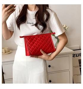 Detailed close-up of a red quilted makeup bag held by a model in a cozy indoor setting