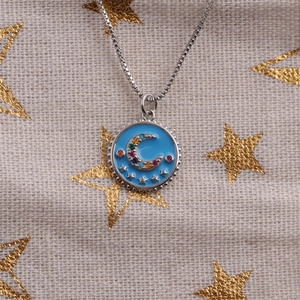 Detailed view of silver necklace with blue enamel moon and star pendant and gems