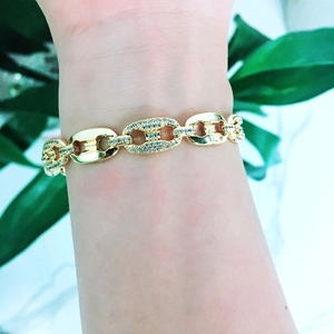 Detail of chunky gold bracelet with pave crystal links on a wrist with plants