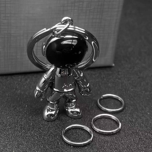 Polished silver astronaut metal keychain with black visor on textured minimalist background