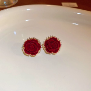 Detailed top view of red velvet rose earrings with white pearl border on white ceramic tray