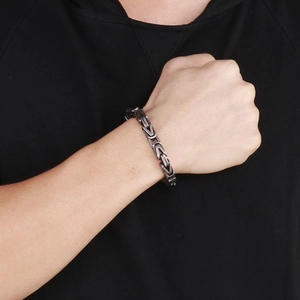 Macro detail of men's stainless steel Byzantine chain bracelet with silver metallic texture
