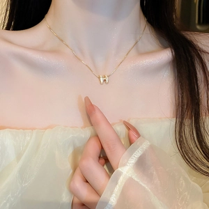 Detail view of a gold-plated necklace featuring a white shell H-shaped pendant on a model