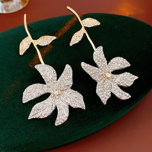 Close-up of silver rhinestone flower earrings with gold leaves on green velvet