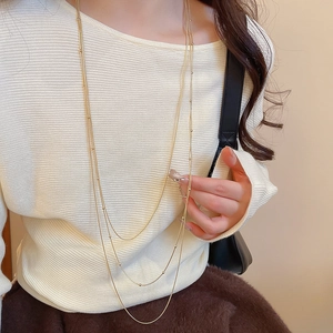 Detail of a triple-layered gold tassel necklace with delicate beads on a knitted sweater