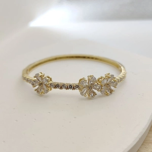 Detailed macro view of a gold-finish clover bangle with sparkling cubic zirconia flower charms