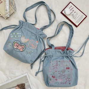 Close-up of bow embroidery and red checkered lining on a light blue denim drawstring tote