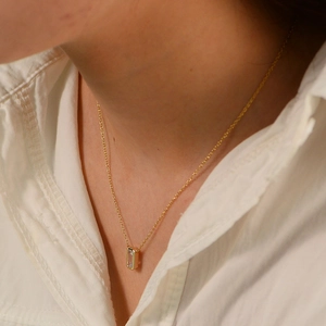 Close-up of minimalist gold chain with a rectangular clear crystal pendant worn by a model