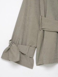 Detailed close-up of grey-green suede top with tie-knot cuffs and belted waist design