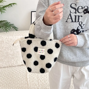 Close-up of white plush handbag with black polka dots and metal zipper closure