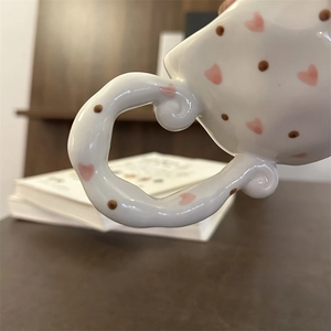 Detail of a handmade ceramic mug featuring a pink heart pattern and a unique twisted handle
