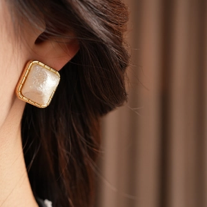 Close-up of a model wearing square gold-plated stud earrings with white mother-of-pearl