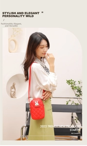 Detail of red quilted crossbody phone bag with cute rabbit clasp worn by model