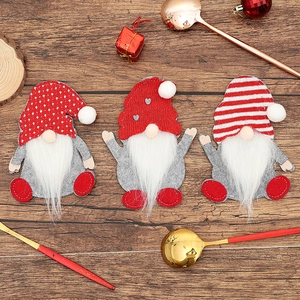 Three Christmas gnome cutlery holders on dark wood table with festive holiday ornaments