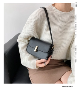 Close-up of a black matte saddle bag with a golden metal buckle on a woman's shoulder